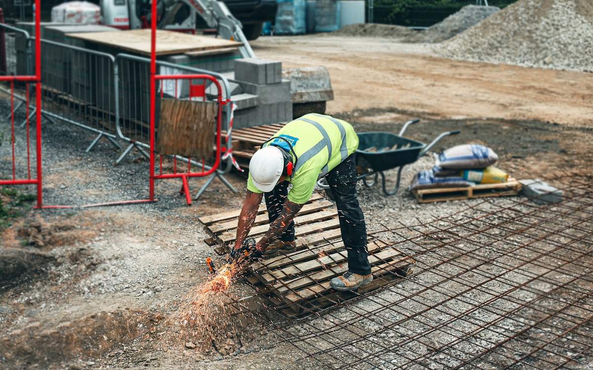 A worker in a high visibility vest cutting steel reinforcement on a building site
