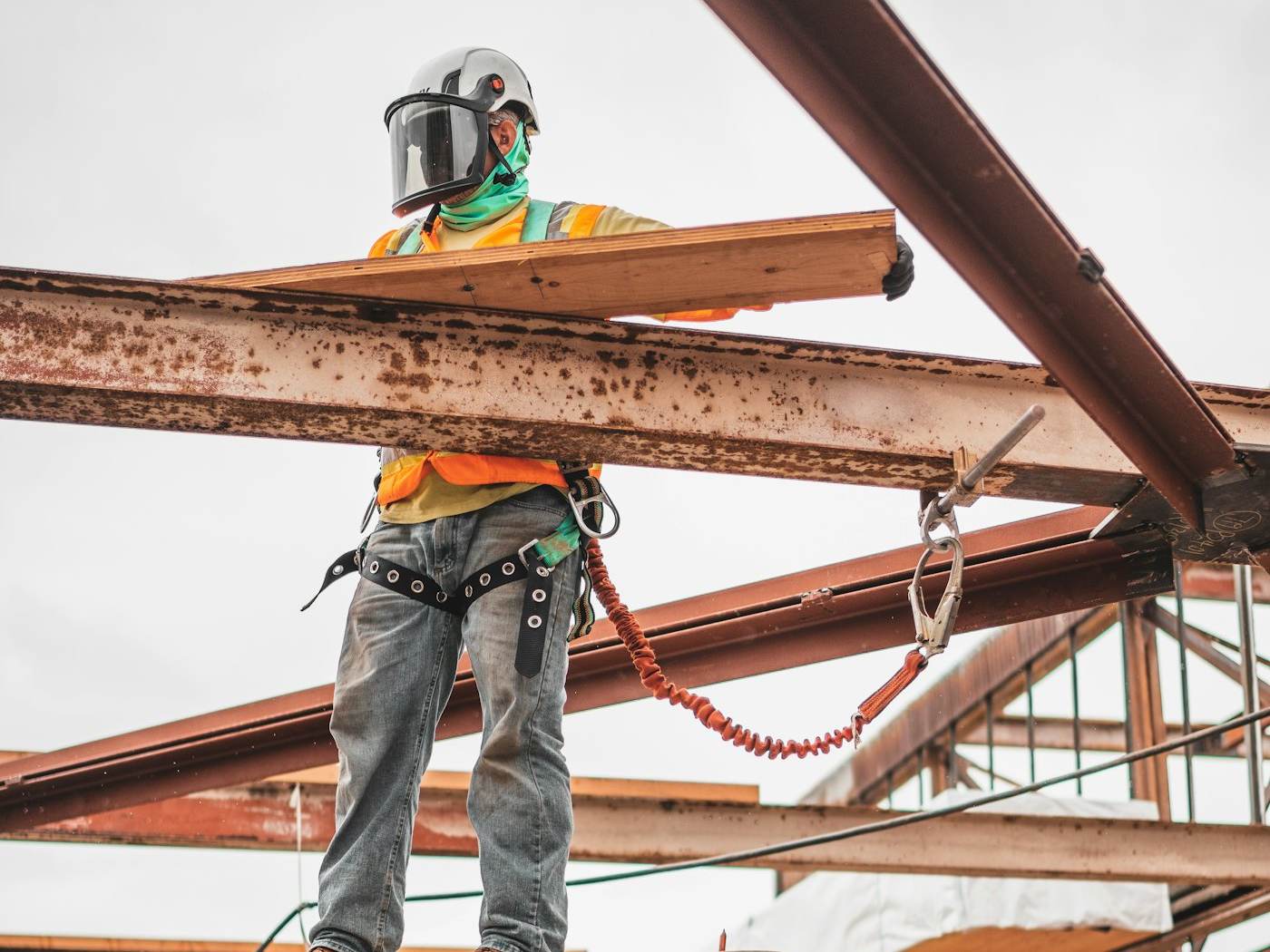 A construction worker in a safety harness working on a steel frame