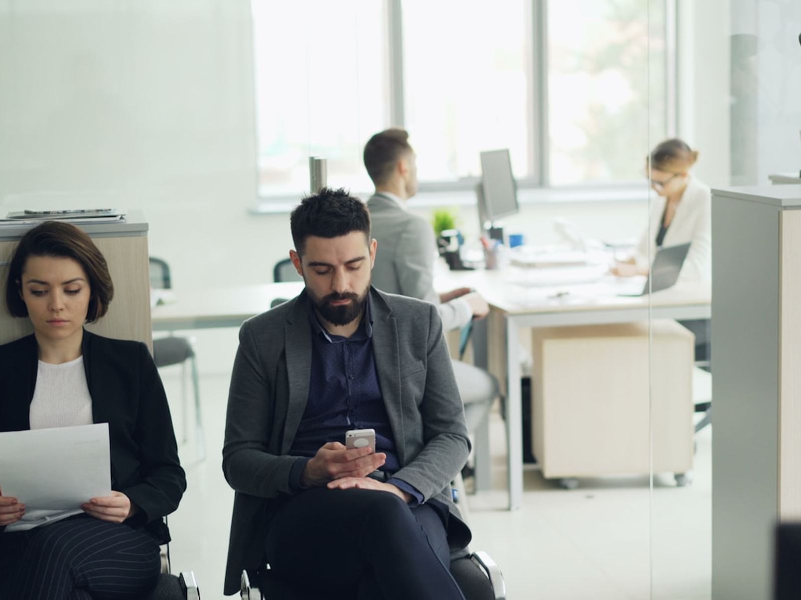 People waiting in an open plan office, one reading a document